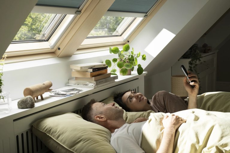 Coppia a letto che usa l'app sotto finestre per tetti con tende elettriche
