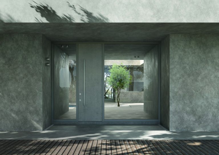 Ingresso in cemento con porta blindata grigia tra due vetrate, cortile sullo sfondo