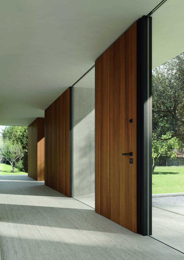 Porta blindata a tutta altezza in legno sotto un portico, giardino sullo sfondo (verticale)