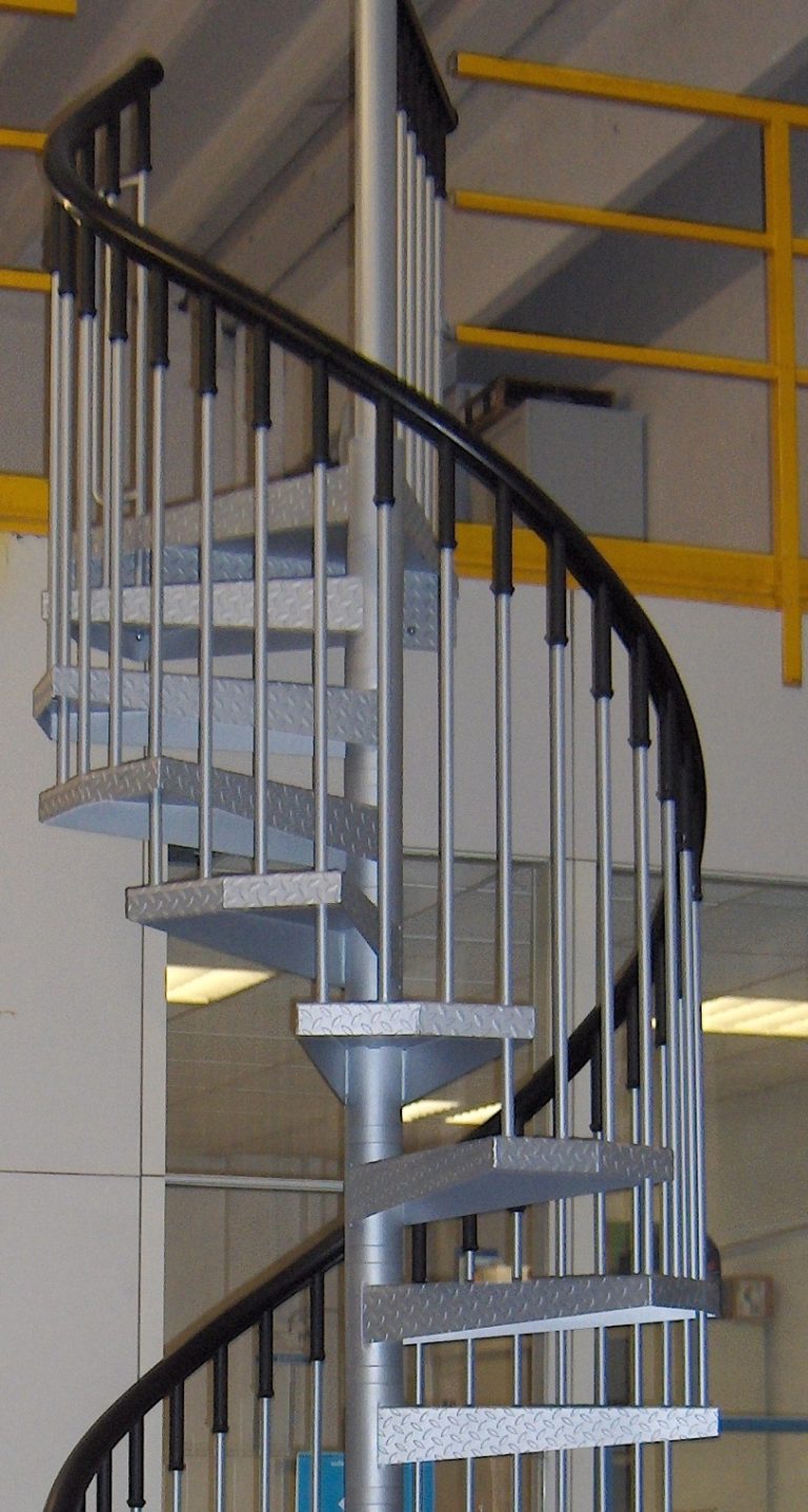 Scala a chiocciola zincata con corrimano nero in ambiente industriale, verticale