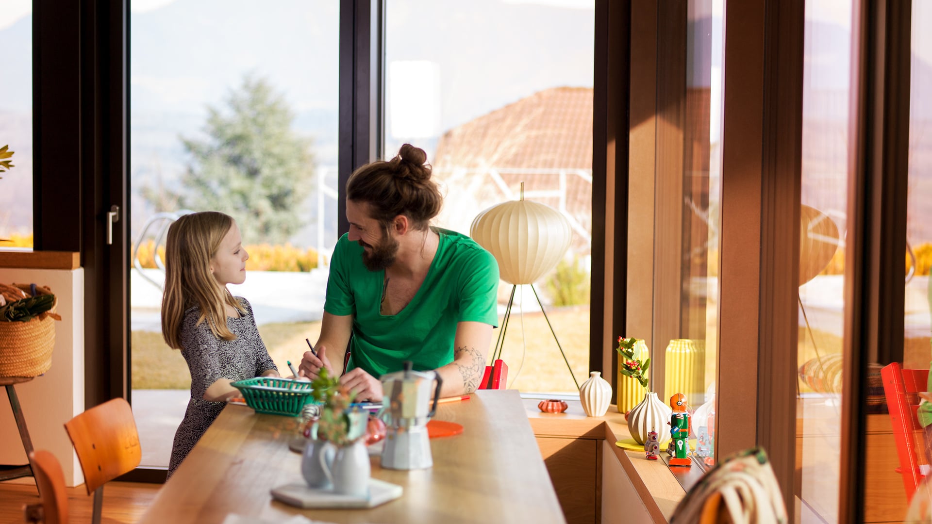 Padre e figlia a tavola in una cucina luminosa con grandi finestre