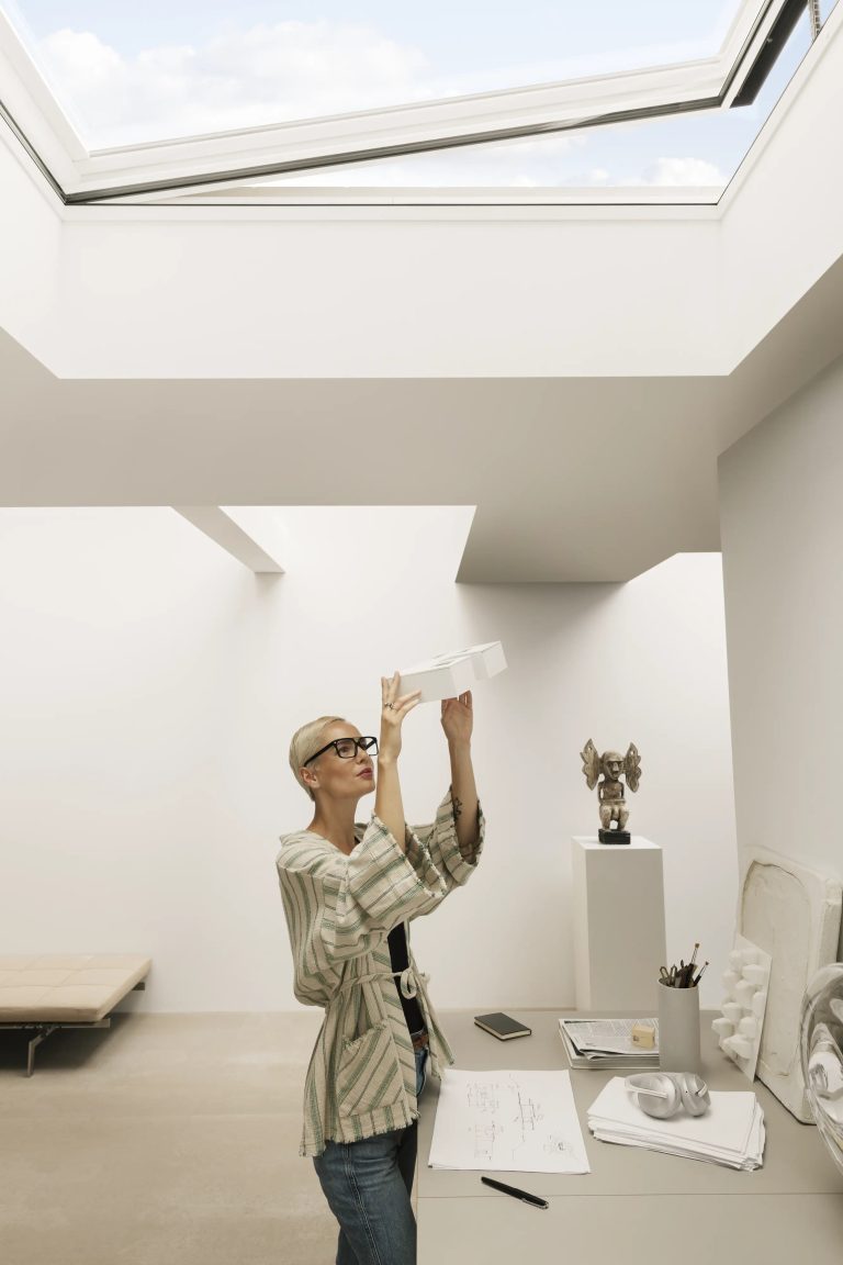 Ambiente bianco illuminato da finestra per tetti piani, donna al lavoro (verticale)
